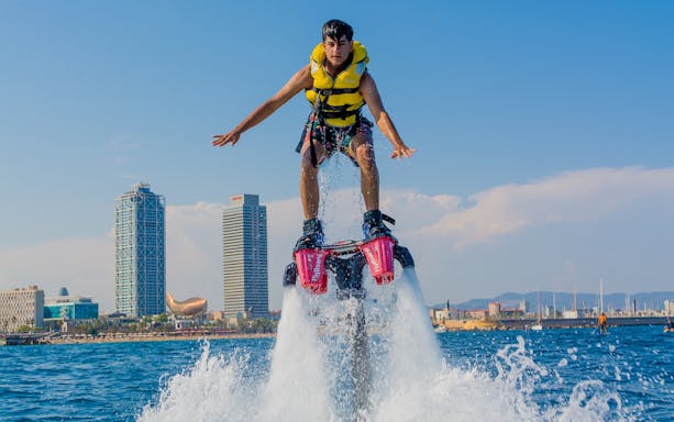 Flyboarder soaring over water with Barcelona skyline in background.