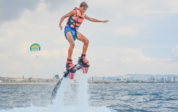 Person flyboarding over water with Barcelona skyline in the background.