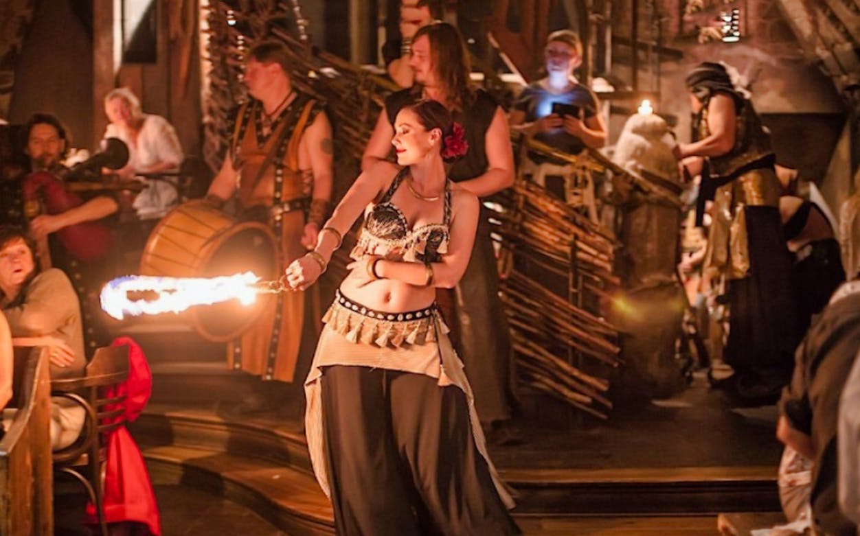 Medieval banquet performer with fire, surrounded by musicians and guests.