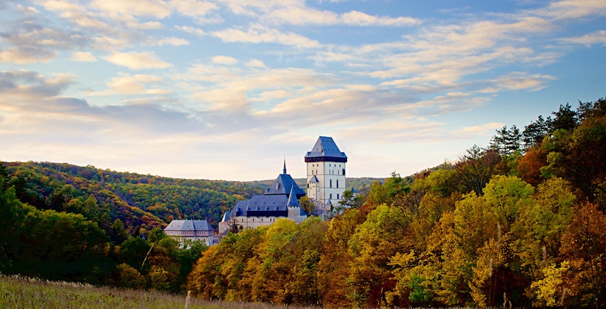 Karlštejn Castle surrounded by autumn trees under a blue sky, Czech Republic.