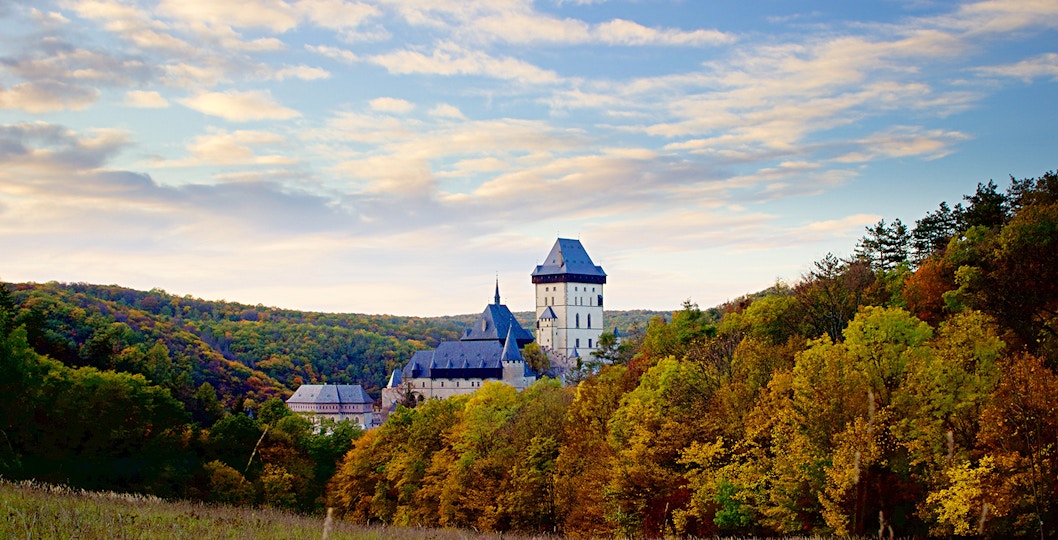 Karlštejn Castle surrounded by autumn trees under a blue sky, Czech Republic.