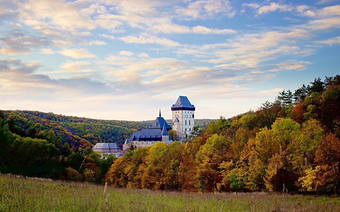 Karlštejn Castle surrounded by autumn trees under a blue sky, Czech Republic.