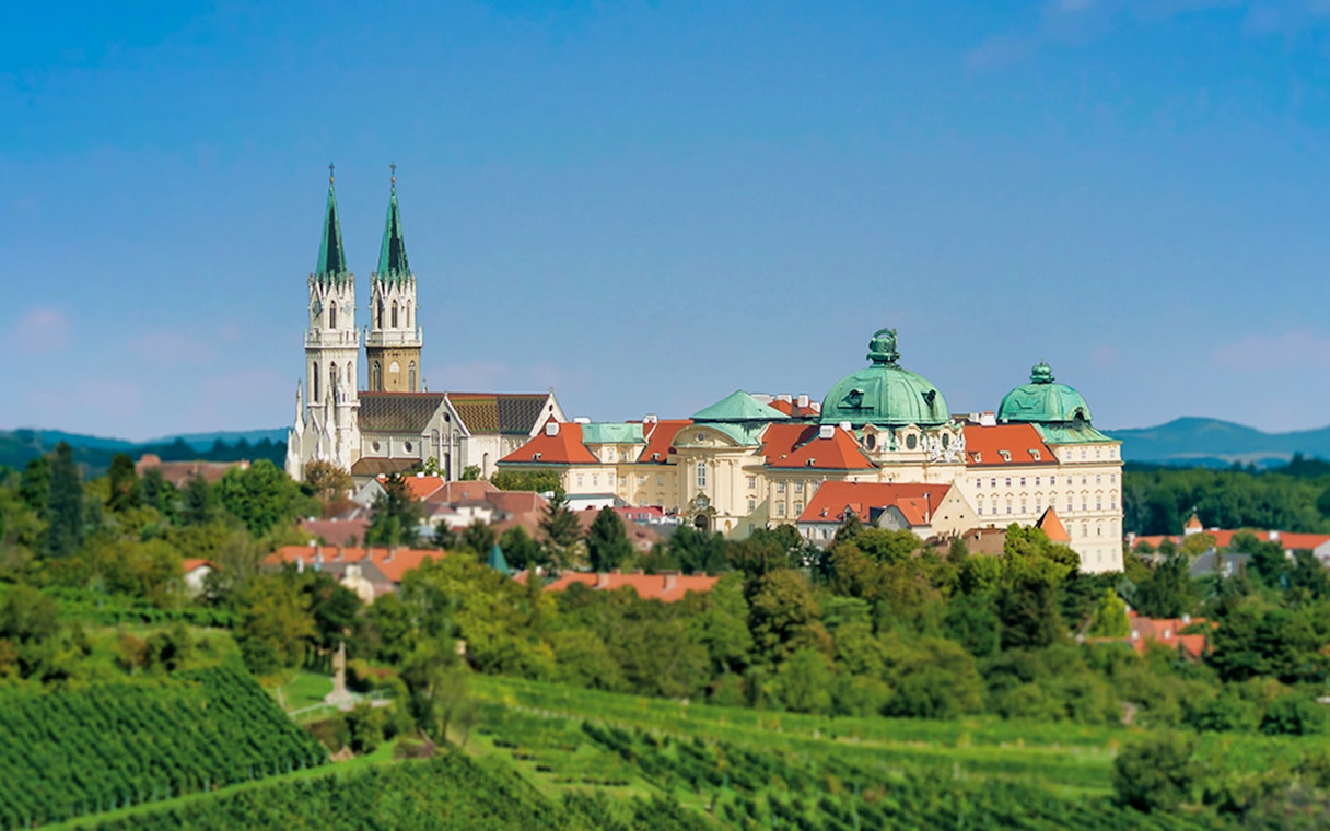 Klosterneuburg Monastery with twin spires and green domes surrounded by lush vineyards.