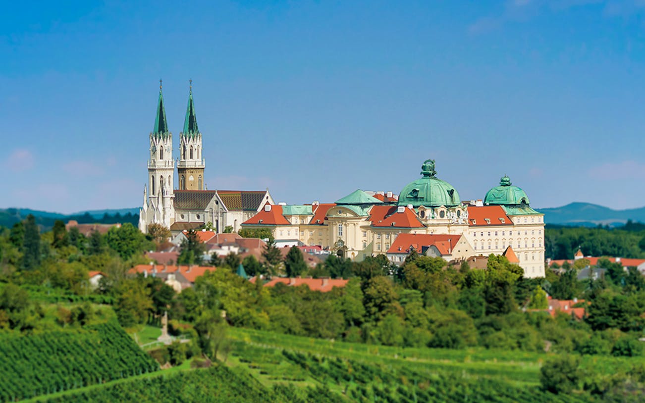 Klosterneuburg Monastery with twin spires and green domes surrounded by lush vineyards.
