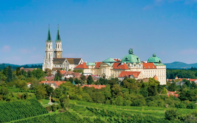 Klosterneuburg Monastery with twin spires and green domes surrounded by lush vineyards.