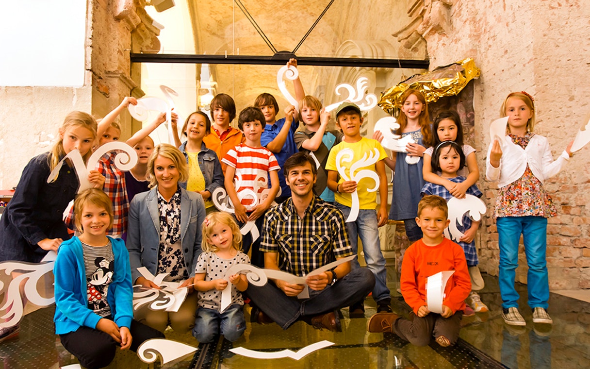 Children and adults holding decorative cutouts at Klosterneuburg Monastery tour.