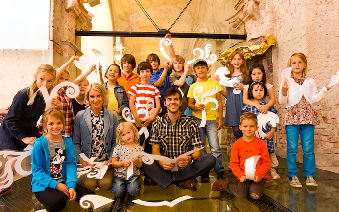 Children and adults holding decorative cutouts at Klosterneuburg Monastery tour.