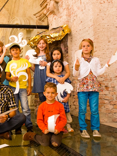 Children and adults holding decorative cutouts at Klosterneuburg Monastery tour.