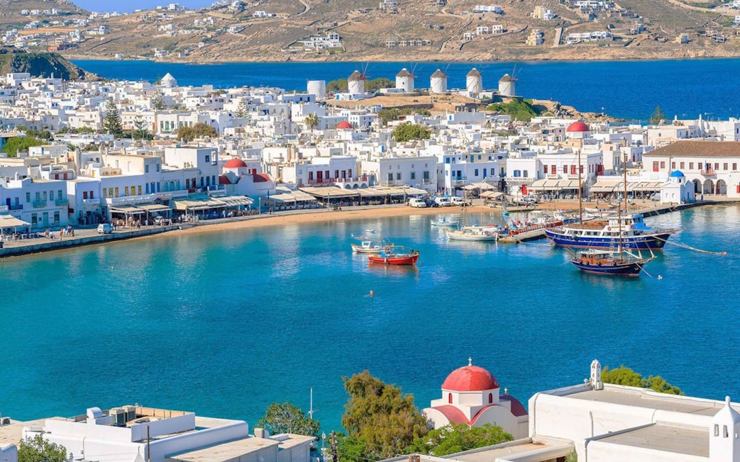 Mykonos harbor with boats and iconic windmills in the background during a 4-hour island cruise.
