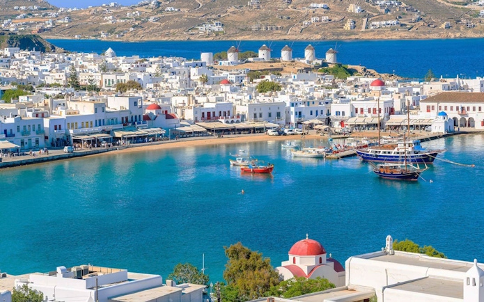 Mykonos harbor with boats and iconic windmills in the background during a 4-hour island cruise.