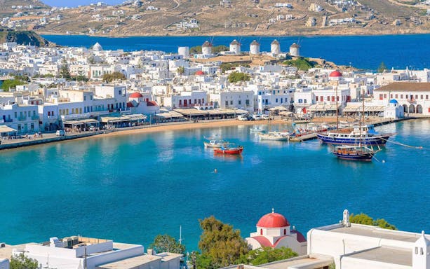 Mykonos harbor with boats and iconic windmills in the background during a 4-hour island cruise.