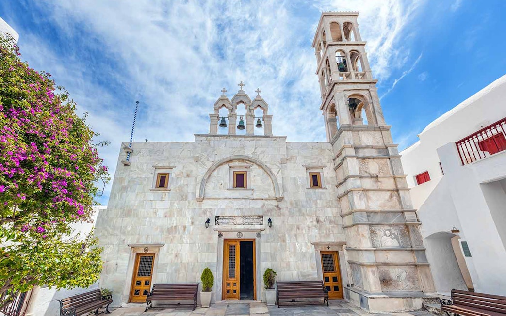 Mykonos church with bell tower and blooming bougainvillea on a sunny day.