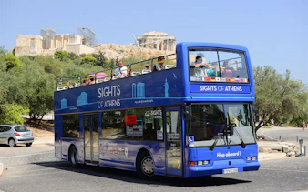 Open-top tour bus in Athens with Acropolis in the background.