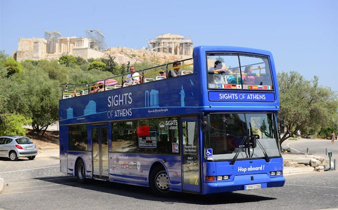 Open-top tour bus in Athens with Acropolis in the background.