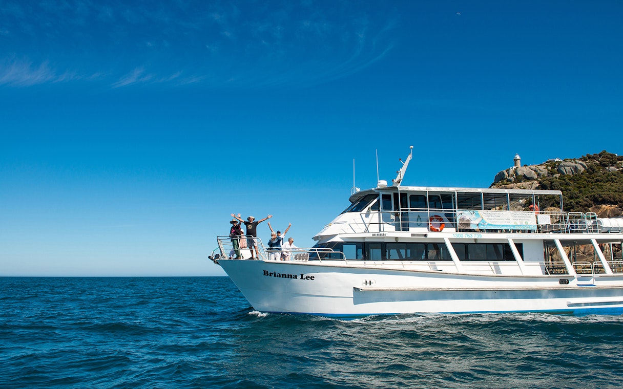Cruise ship with passengers enjoying Wilsons Prom Whale Adventure near coastal cliffs.