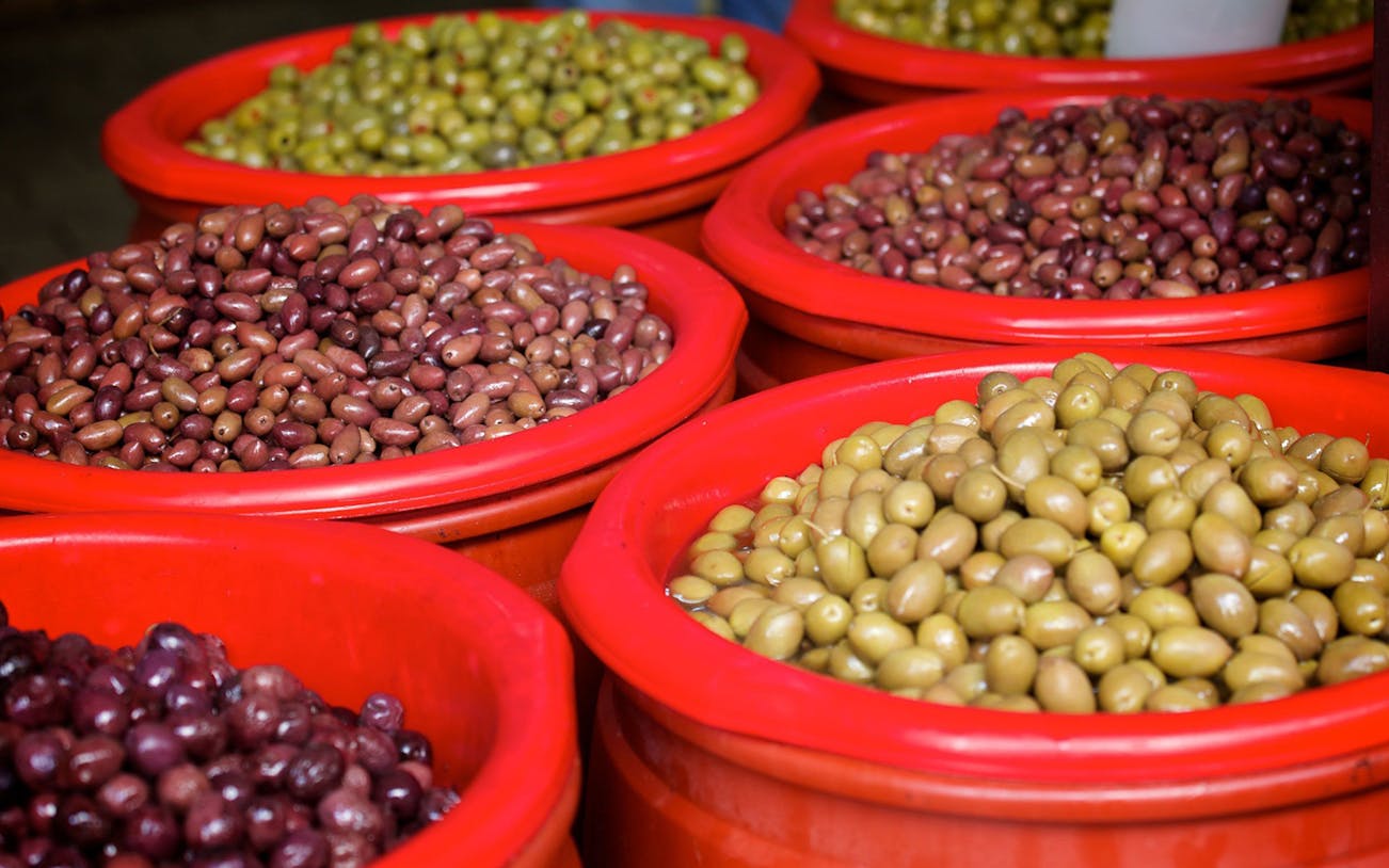 Variety of olives in red bowls at Athens market during food tour.