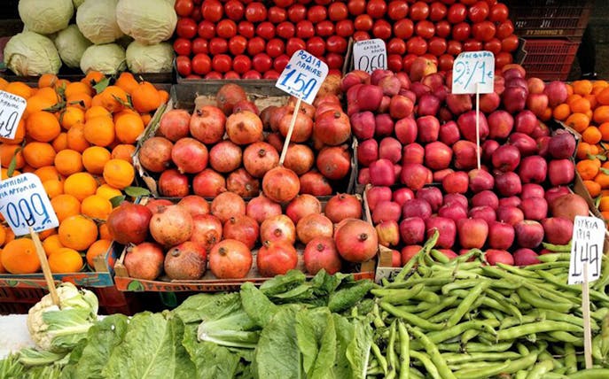 Market stall with pomegranates, apples, oranges, and greens in Athens.