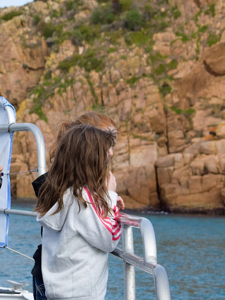 Tourists on a boat admire rocky cliffs during Cape Woolamai morning cruise, Phillip Island.