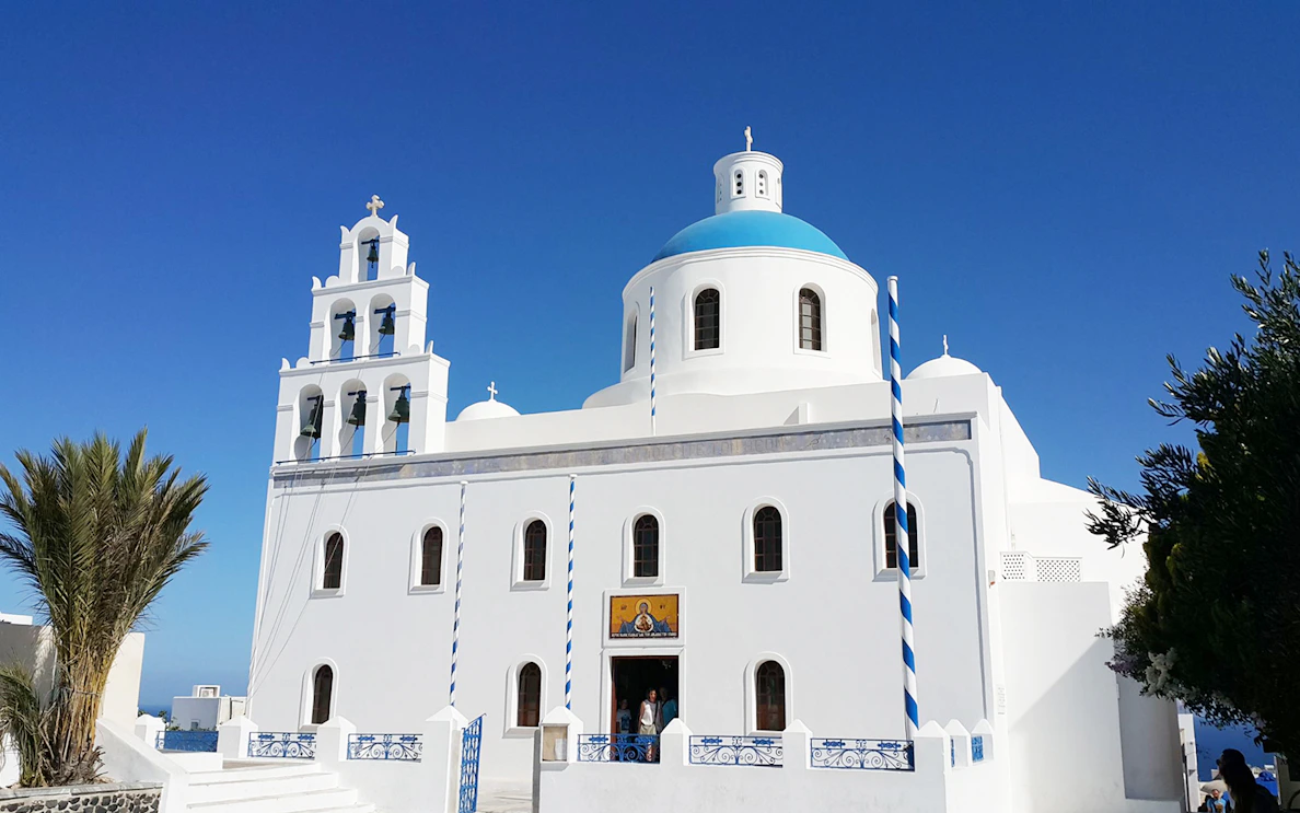 White church with blue dome and bell tower in Santorini, Greece, on a private tour with wine tasting.