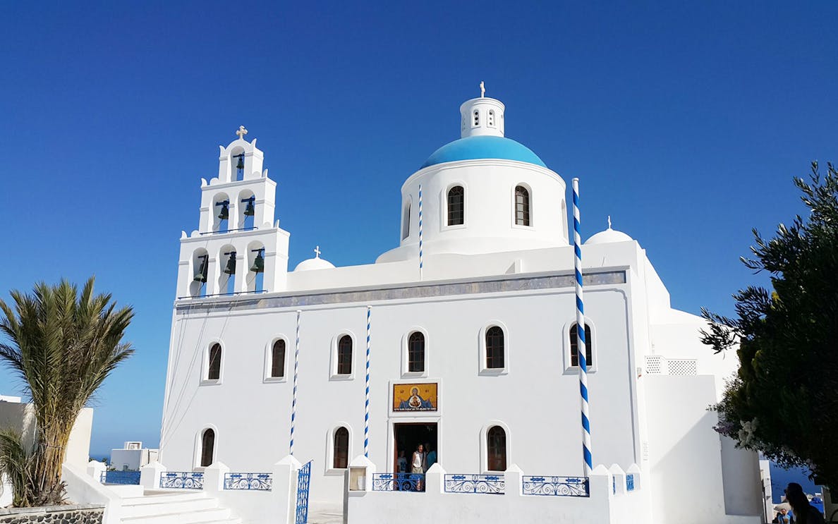 White church with blue dome and bell tower in Santorini, Greece, on a private tour with wine tasting.