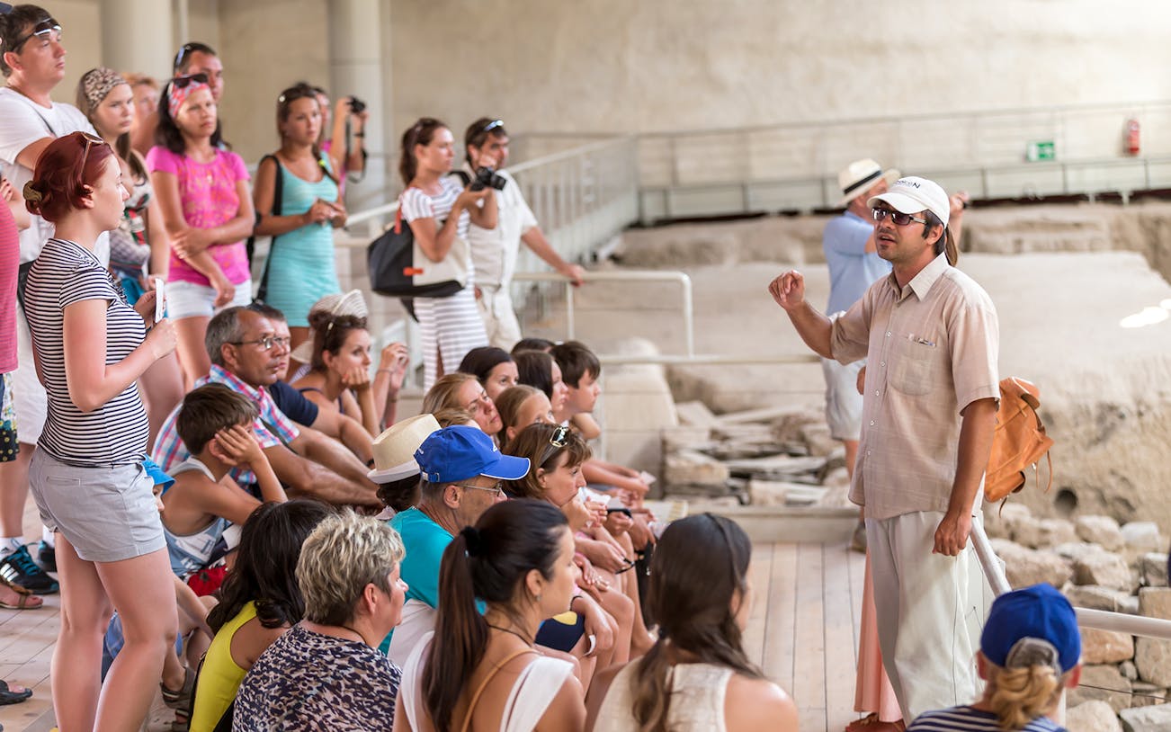 Tour group listening to a guide at an archaeological site in Santorini.