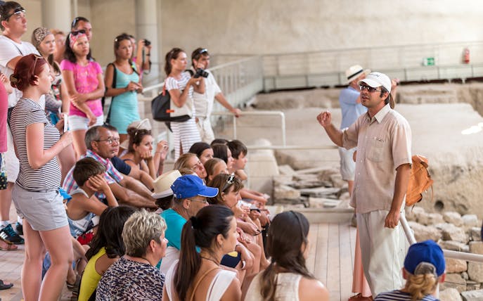 Tour group listening to a guide at an archaeological site in Santorini.