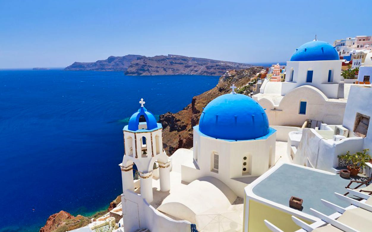 Santorini's blue-domed churches overlooking the Aegean Sea, part of a day trip with wine museum and Oia sunset.