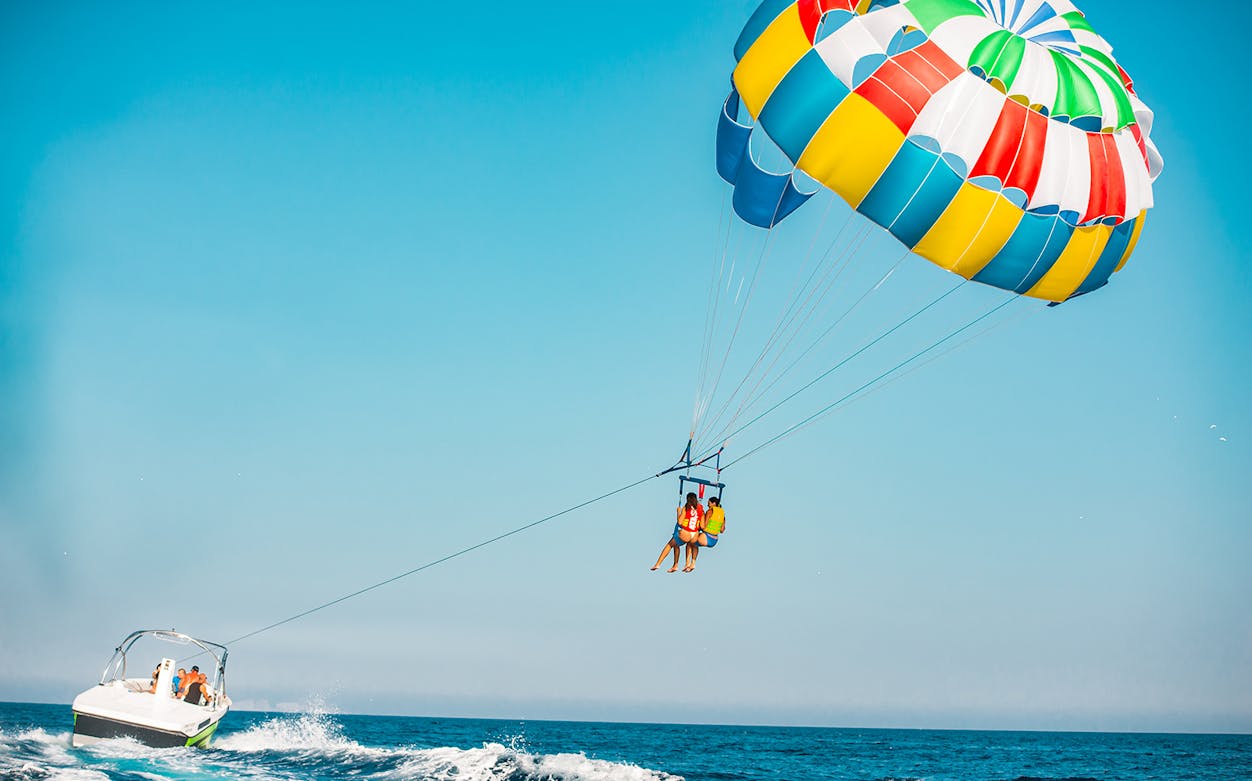 Parasailing over Super Paradise Beach with colorful parachute and boat.