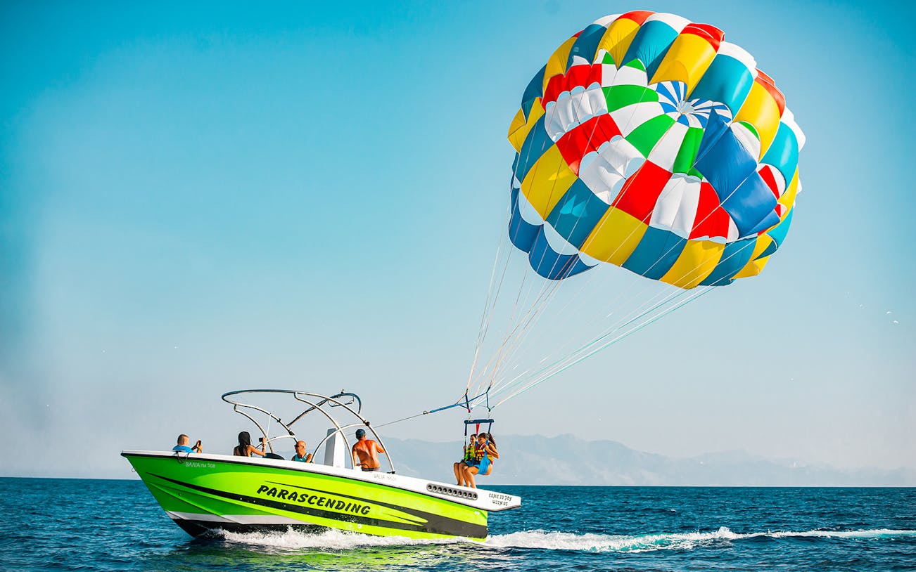 Parasailing over Super Paradise Beach with colorful parachute and boat.