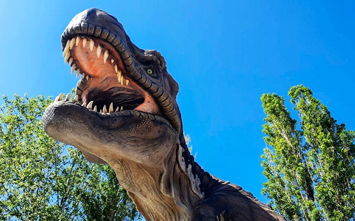 Dinosaur sculpture at Acquario di Cattolica against a clear blue sky.