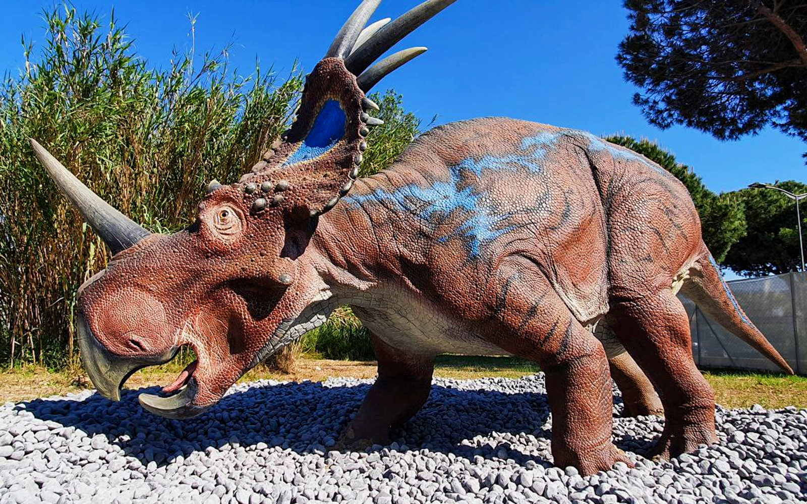 Dinosaur sculpture at Acquario di Cattolica, Italy, surrounded by greenery.