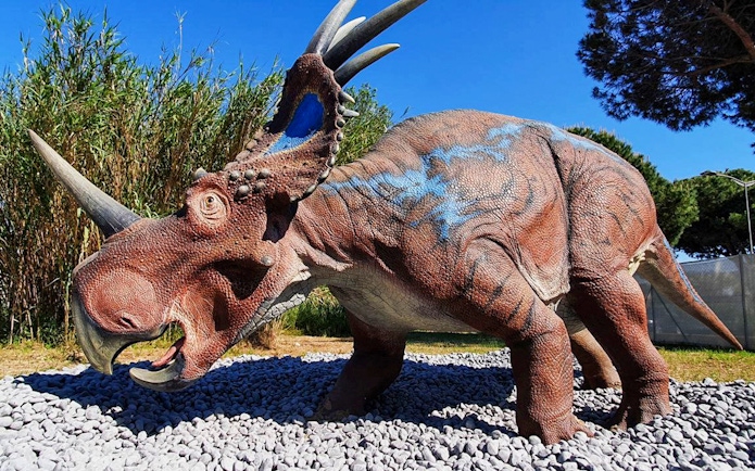 Dinosaur sculpture at Acquario di Cattolica, Italy, surrounded by greenery.