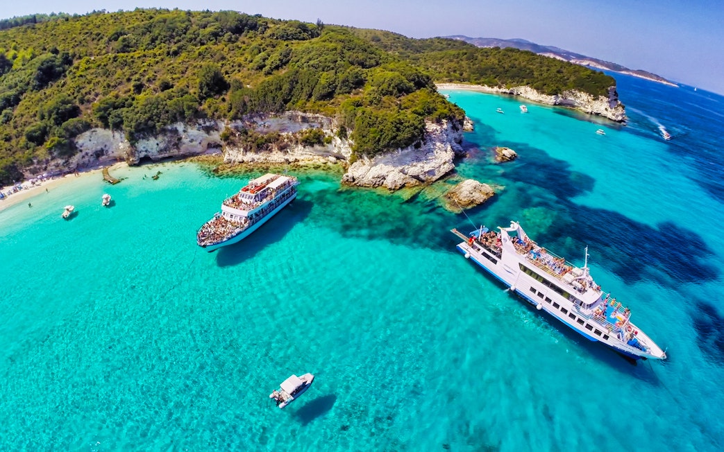 Cruise ships near Paxos Antipaxos Blue Caves with clear turquoise water and lush coastline.