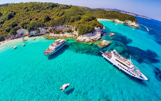 Cruise ships near Paxos Antipaxos Blue Caves with clear turquoise water and lush coastline.