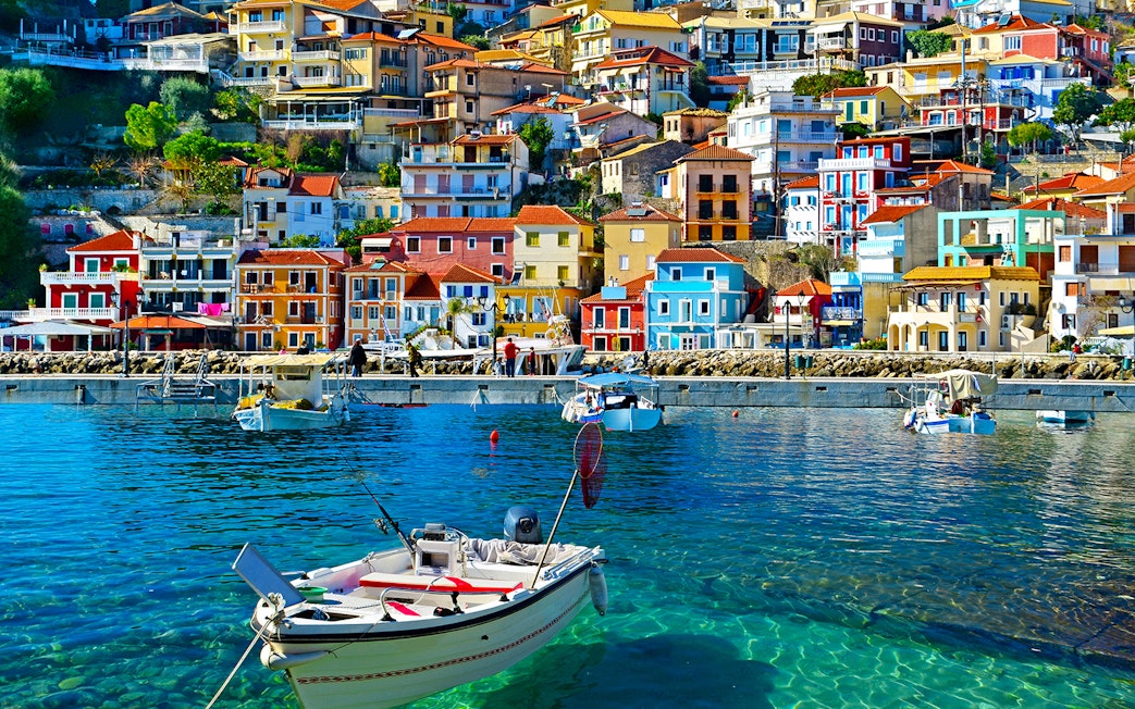 Colorful houses along Parga's waterfront with boats in clear blue water, Greece.