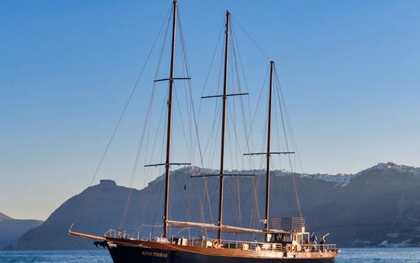 Sailing boat on Santorini sunset tour with cliffs in the background.