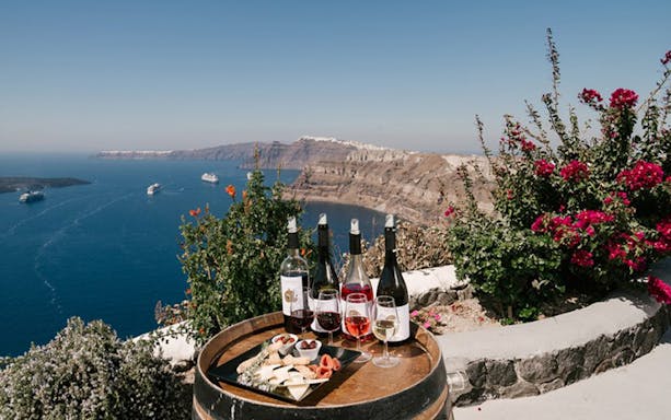 Wine tasting setup overlooking Santorini caldera with cruise ships in the distance.