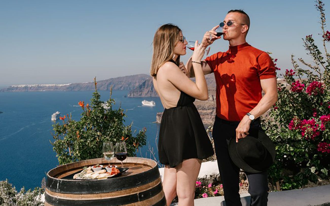 Couple enjoying wine with a view of the Santorini caldera and cruise ships.
