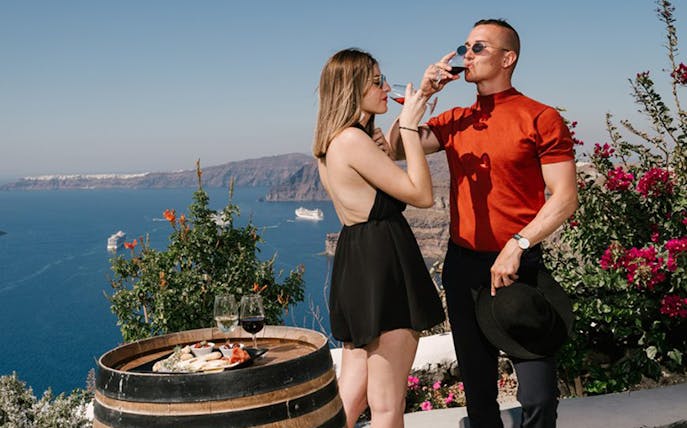 Couple enjoying wine with a view of the Santorini caldera and cruise ships.