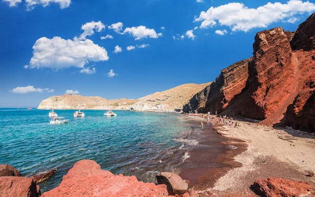 Red beach with volcanic cliffs and boats in Santorini, Greece, on a Volcano Sightseeing Tour.