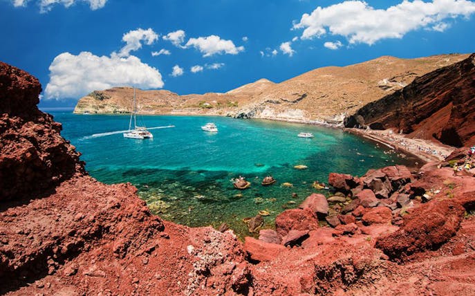Catamarans in turquoise waters near red volcanic cliffs, Santorini.