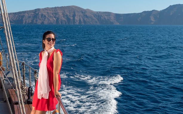 Woman enjoying a boat tour with volcanic cliffs in the background, Santorini, Greece.