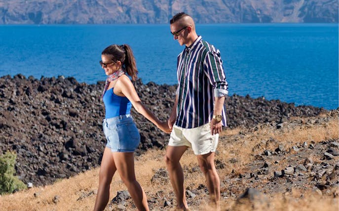 Couple walking on volcanic terrain with ocean view during sightseeing tour.