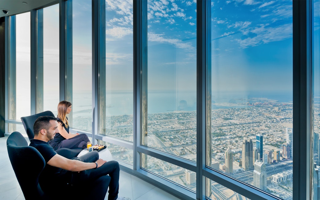 Visitors enjoying city view from Burj Khalifa with coffee and pastries.