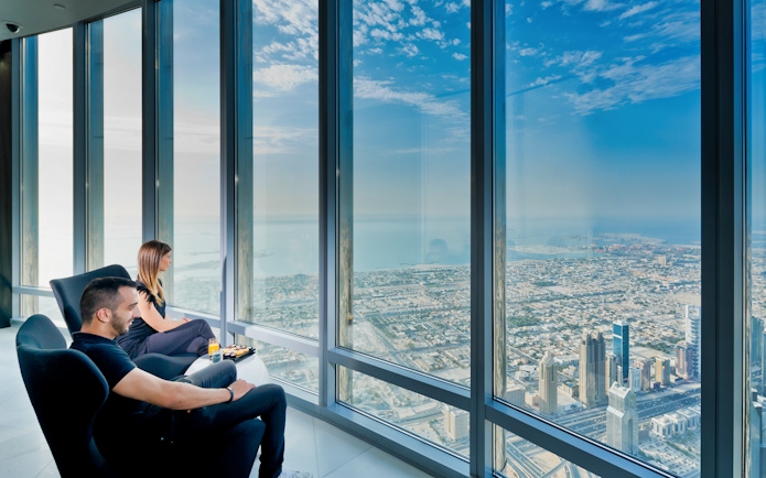 Visitors enjoying city view from Burj Khalifa with coffee and pastries.
