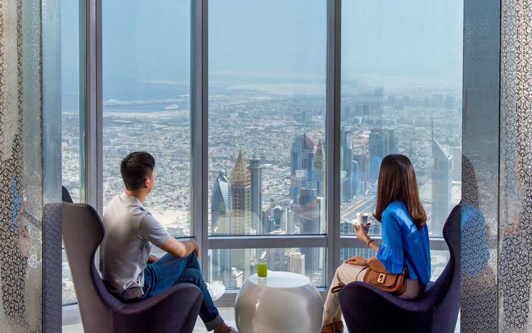 Visitors enjoying city view from Burj Khalifa café with coffee, Dubai skyline visible.