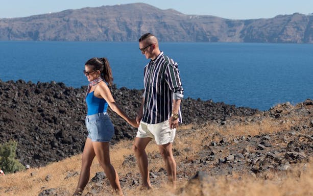 Couple walking on Santorini volcano with caldera view.