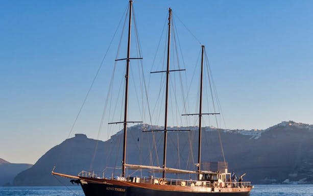 Sailing ship near Santorini cliffs during Full Day Santorini Volcano & Oia Sunset Tour.