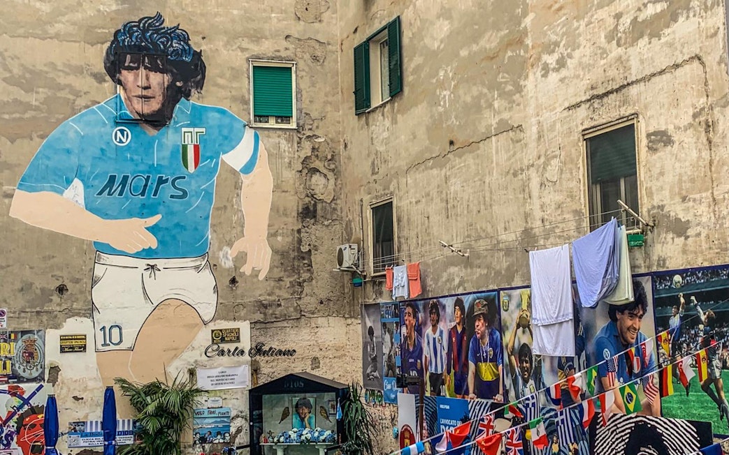 Mural of Diego Maradona in Naples, Italy, with surrounding tribute photos.