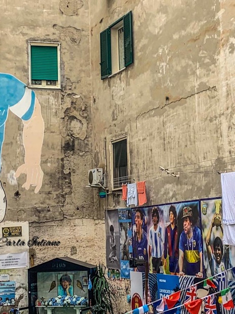 Mural of Diego Maradona in Naples, Italy, with surrounding tribute photos.